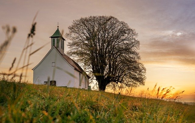 Kirche auf einem Feld bei Sonnenuntergang: Kirchenbanken unterstützen vor allem kirchliche und karitative Einrichtungen finanziell