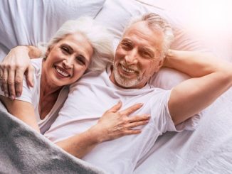 Älteres Paar, das gemeinsam glücklich in einem weißen Bett liegt: Auch ältere Menschen können einen Kredit für Rentner über 70 Jahren erhalten!