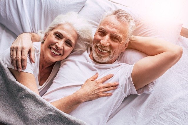 Älteres Paar, das gemeinsam glücklich in einem weißen Bett liegt: Auch ältere Menschen können einen Kredit für Rentner über 70 Jahren erhalten!