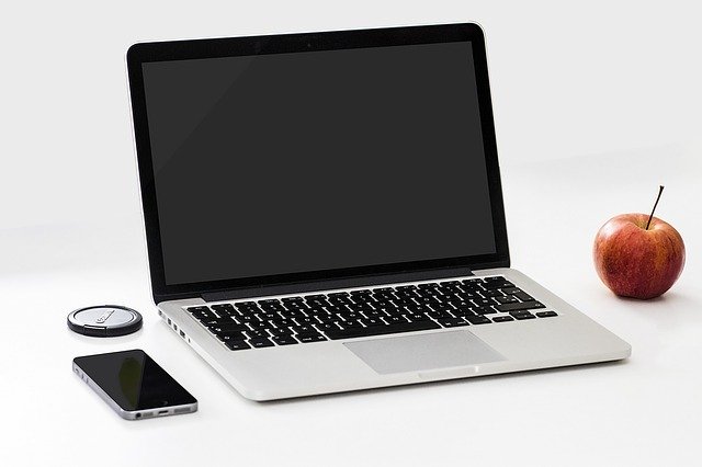 Smartphone, Macbook Pro und roter Apfel auf einem weißen Schreibtisch: Wenn Sie 14000 Euro benötigen, dann können Sie bequem vom eigenen Schreibtisch aus einen günstigen 14000 Euro Kredit online beantragen!