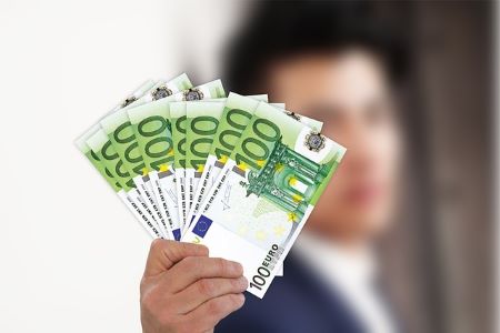 Junger Mann im Business-Anzug mit mehreren 100 Euro Banknoten in der rechten Hand: Endlich wieder liquide dank einem günstigen 17000 Euro Kredit!
