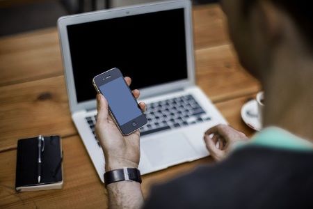 Mann am Laptop mit Smartphone in der Hand, der gerade im Begriff ist, einen 19000 Euro Kredit zu beantragen