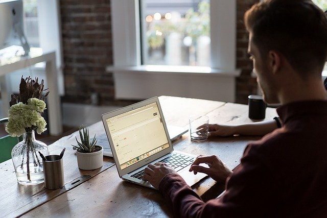 Junger Mann, der an einem Tisch sitzt und am Laptop nach einem günstigen 30000 Euro Kredit sucht