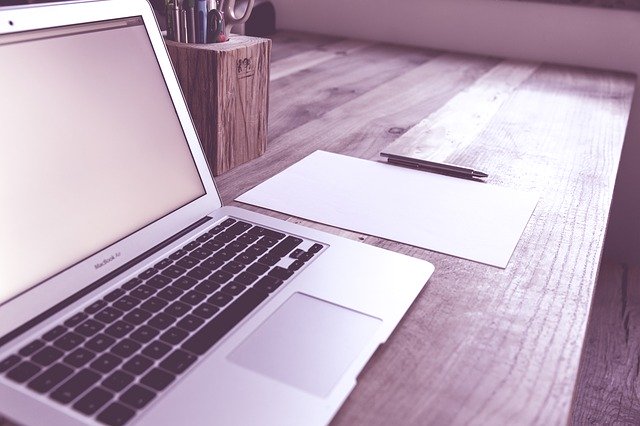 Macbook, weißes Blatt Papier und Stift auf einem Schreibtisch: Sie benötigen einen günstigen 40000 Euro Kredit? Beantragen Sie diesen ganz bequem von Zuhause aus: online!