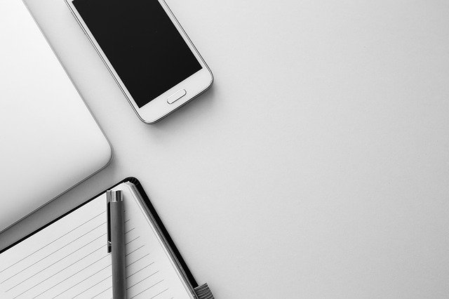 Laptop, Smartphone, Notizbuch und Stift auf einem Schreibtisch: Wenn Sie ein großes Darlehen benötigen, können Sie heutzutage ganz leicht online einen 75000 Euro Kredit beantragen!