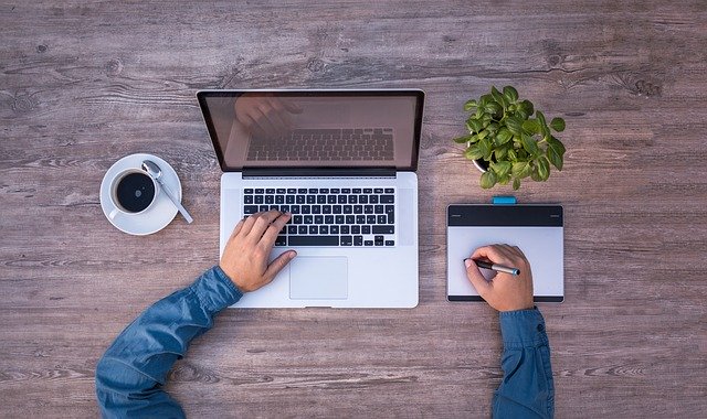 Tasse Kaffee, Laptop, Pflanze und Notizbuch auf einem Tisch. Junger Mann mit Stift vor dem Laptop sitzend: Wenn Sie einen günstigen Kredit benötigen sollten, dann können Sie noch heute den Bank of Scotland Kredit online beantragen!