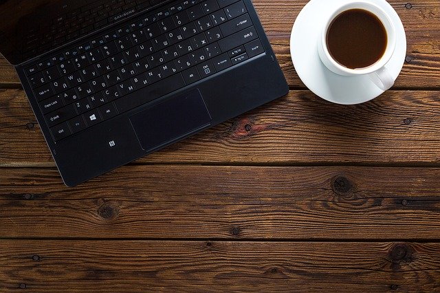 Laptop und weiße Tasse mit Kaffee auf einem Holztisch: Wenn Sie auf der Suche nach einem bonitätsunabhängigen Darlehen sind, sollten Sie sich den Deutsche Kreditbank Kredit (DKB Kredit) mal genauer ansehen!