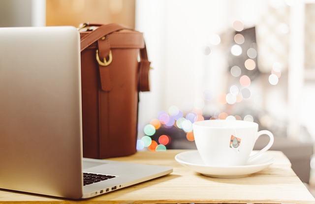 Grauer Laptop, weiße Tasse mit Tee und braune Tasche auf einem Schreibtisch: Wenn Sie einen Ratenkredit für private Zwecke benötigen, dann können Sie noch heute ein faires DKB Privatdarlehen bequem online beantragen!