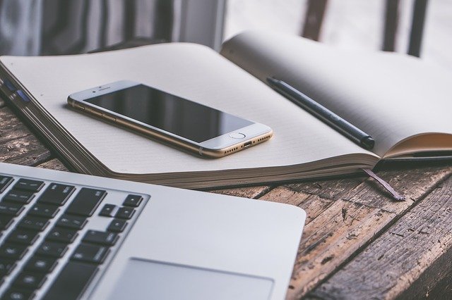 Laptop, Smartphone, Notizblock und Stift auf einem hölzernen Tisch: Wenn Sie einen fairen Kredit benötigen, ist der Santander Kredit evtl. genau der richtige für Sie!?