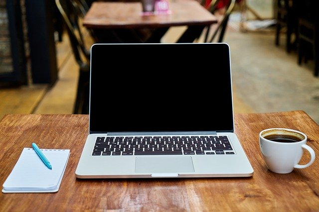 Notizblock und Stift, Laptop und Tasse Kaffee auf einem Tisch: Wenn Sie einen Kredit online beantragen möchten, wäre eventuell der flexible SWK Bank Kredit eine gute Option für Sie!?
