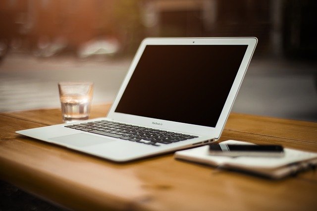 Weißer Laptop auf dem Tisch, daneben ein Glas Wasser, ein Notizblock und ein Stift: Beantragen Sie noch heute Ihren Targobank Kredit mit Wunschrate online!