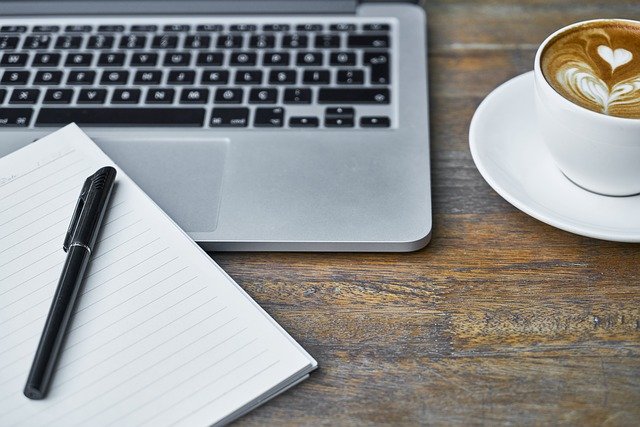 Notizbuch, Stift, Laptop und Tasse Kaffee auf einem Tisch: Wenn Sie gerade auf der Suche nach einem günstigen Kredit sind, dann schauen Sie sich am besten mal den HypoVereinsbank Kredit ab nur 1,59% eff. p.a. genauer an! 